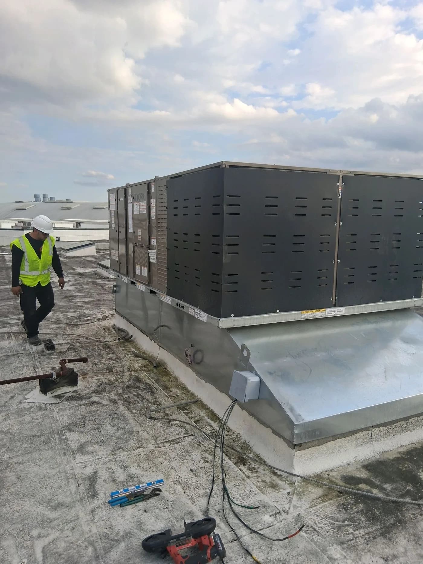 Blue Works technician in safety gear beside a YORK commercial rooftop unit during installation